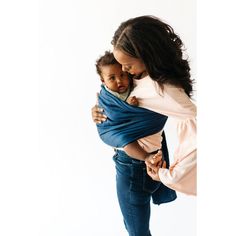 a woman holding a baby wrapped in a blue wrap while standing against a white background