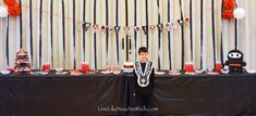 a young boy standing in front of a table with cake and decorations on the table