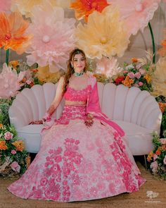 a woman in a pink dress sitting on a white couch with large paper flowers behind her