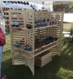 a wooden shelf with jars and cups on it at an outdoor event in the grass