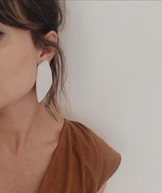 a woman wearing large white earrings and a brown top is standing in front of a wall