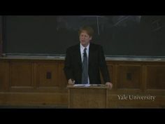 a man standing at a podium in front of a blackboard