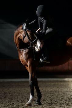 a woman riding on the back of a brown horse in an indoor arena at night