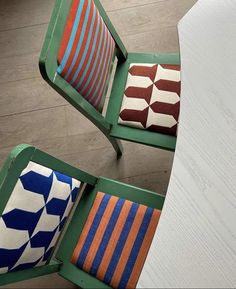 two green chairs with colorful pillows on them sitting next to each other in front of a white table