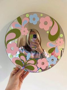 a woman taking a selfie in front of a mirror with flowers painted on it