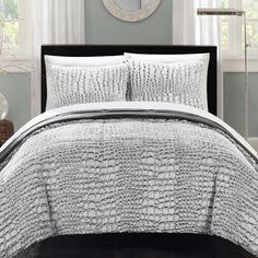 the comforter is made up with white and gray bedding, along with a round mirror