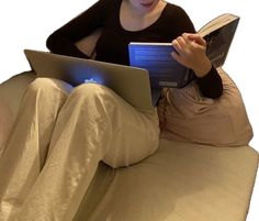 a woman sitting on a couch with a laptop and book in her lap while reading