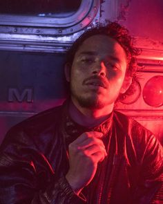 a man in a leather jacket standing next to a wall with red lights on it