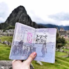 a person holding up a passport in front of a mountain