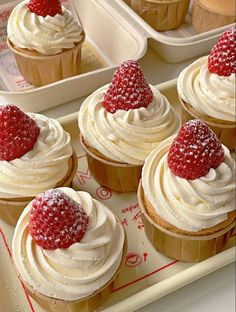 several cupcakes with white frosting and strawberries on top are shown in trays