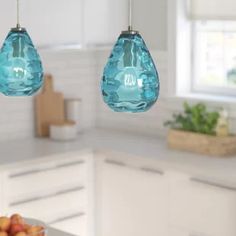 two blue glass pendant lights hanging from a kitchen ceiling over a bowl of fruit on the counter