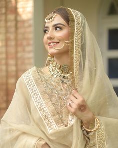 a woman wearing a white and gold bridal outfit with jewelry on her head, standing in front of a brick building