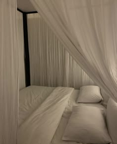 a bed with white sheets and pillows in a room that has curtains on the walls