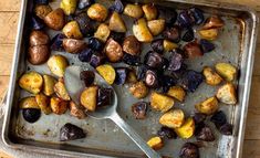 a pan filled with cooked potatoes and other vegetables on top of a wooden table next to a spoon