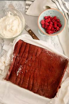 chocolate cake with raspberries on top and whipped cream in the bowl next to it