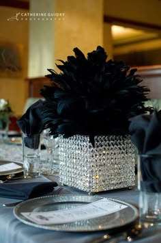 the centerpieces are adorned with black feathers and crystal beaded napkins, along with silver plates