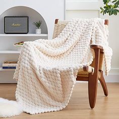 a white blanket sitting on top of a wooden chair next to a potted plant