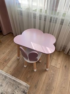 a pink table sitting on top of a wooden floor next to a white curtained window