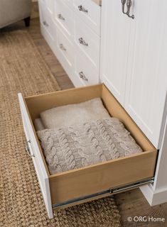 an open drawer in the middle of a carpeted floor next to white cabinets and drawers