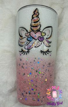 a pink and white tumbler with a unicorn on it's side sitting on a fluffy surface