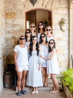 a group of women standing next to each other in front of a stone building with sunglasses on