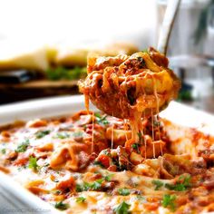 a spoon full of pasta being lifted from a casserole dish with meat and cheese