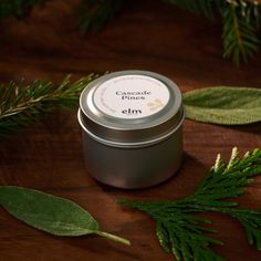 an empty tin candle sitting on top of a wooden table next to some green leaves