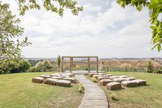 a wooden path leading to a stone structure in the middle of a field with hay bales