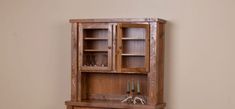 a wooden cabinet with glass doors on the top and bottom shelf, in front of a beige wall