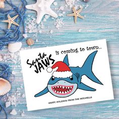 a christmas card with a shark wearing a santa hat on it's head, surrounded by seashells and starfish