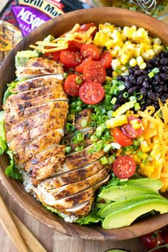 a wooden bowl filled with chicken, black beans, corn, tomatoes and avocado