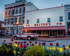 an old truck is parked in front of a store with tulips and other flowers