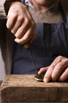 a man with an apron is using a knife to sharpen a piece of wood