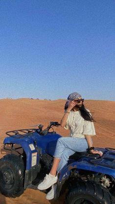 a woman sitting on the back of a blue four wheeler in the middle of desert