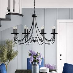 a black chandelier hangs over a dining room table with blue chairs and purple flowers