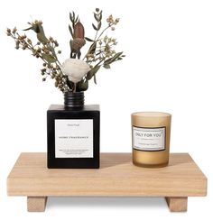 a candle and vase with flowers on a wooden shelf next to each other in front of a white background