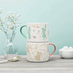 three coffee mugs sitting on top of a table next to a vase with flowers