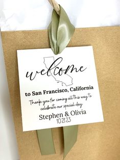 a welcome sign is attached to a brown paper bag with a green ribbon on it