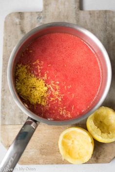 a pan filled with red liquid next to sliced lemons