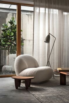 a white chair sitting in front of a window next to a table with a lamp on it