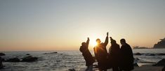 three people standing on the beach with their arms up in the air as the sun sets