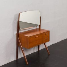 a mirror sitting on top of a wooden dresser next to a white wall and black floor