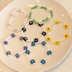 four bracelets made out of plastic beads and flowers on a white plate with marble counter top