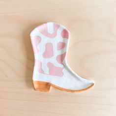 a cookie shaped like a boot with pink and white designs on the front, sitting on a wooden surface