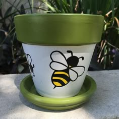 a green and white flower pot with a bee painted on the side sitting on a plate