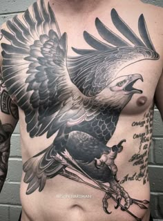 a bald man with an eagle tattoo on his chest and arm is standing in front of a brick wall