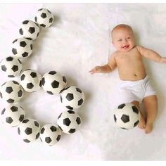 a baby laying next to some balls on a white sheet with the letter c spelled out