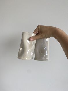 a hand holding two white cups in front of a white wall with one being held up by the other