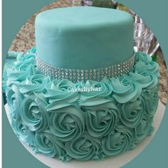 there is a cake with blue frosting and roses on the top, along with a crystal bow