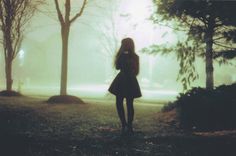 a woman standing in the middle of a park on a foggy day with her phone up to her ear